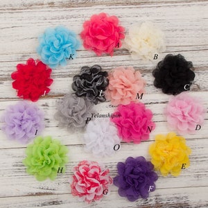 May include: Assortment of 15 handmade fabric flower embellishments in various colors, including pink, red, white, blue, yellow, green, purple, and black. The flowers are made of layered fabric and have a ruffled appearance.