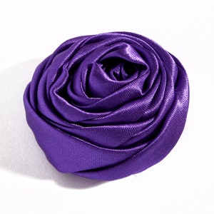 May include: A large, purple satin rose flower. The rose is made of fabric and has a soft, velvety texture.