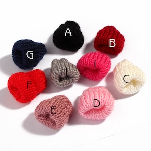 Könnte beinhalten: Sortiment von zehn Mini-Strickmützen in verschiedenen Farben, darunter Rot, Pink, Weiß, Grau, Schwarz und Blau. Die Mützen sind alle klein und haben ein schlichtes Design.