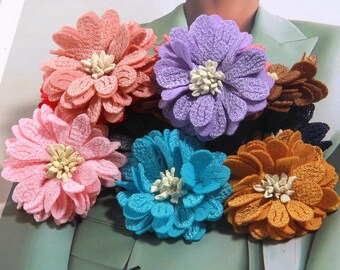 Puede incluir: Una colección de adornos florales de tela en varios colores, incluyendo rosa, melocotón, morado, azul y naranja. Cada flor tiene un diseño de pétalos texturizados y un centro de color crema. La palabra "CELINE" es visible en el fondo.