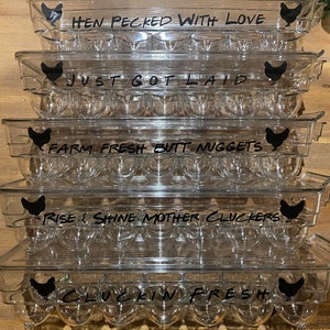 May include: Five clear plastic egg cartons stacked on top of each other. Each carton has a black silhouette of a chicken and a funny saying about eggs. The sayings are: "Hen Pecked With Love", "Just Got Laid", "Farm Fresh Butt Nuggets", "Rise & Shine Mother Cluckers", and "Cluckin Fresh".