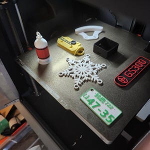 Może przedstawiać: Biała, trójwymiarowa ozdoba w kształcie płatka śniegu, żółty brelok z czarno-białym logo, czerwono-biała ozdoba w kształcie butelki, biały element plastikowy, czarne pudełko, zielona tablica rejestracyjna z napisem "E 47-35" oraz czerwono-czarna naklejka z napisem "GS300".