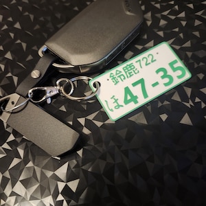May include: A black car key with a silver key ring attached to a green tag with the text "登録 722" and "ま 47-35".