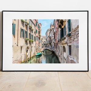 K&ouml;nnte beinhalten: Ein schmaler Kanal in Venedig, Italien, mit farbenfrohen Geb&auml;uden an den Seiten. Ein kleines gr&uuml;nes Boot befindet sich im Wasser, und eine Br&uuml;cke &uuml;berquert den Kanal in der Ferne.