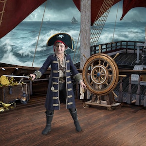 May include: A young pirate dressed in a blue and gold costume stands on a wooden ship deck. The pirate is holding a sword and wearing a black pirate hat with a skull and crossbones. The ship's wheel is visible in the background.