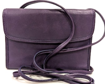 May include: A deep purple leather crossbody bag with a flap closure and a long, thin strap. The bag has a rectangular shape and appears to be made of smooth leather. The strap is also purple and is attached to the sides of the bag.