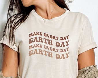 Puede incluir: Una camiseta blanca con el texto "Make Every Day Earth Day" impreso en letras marrones y naranjas.