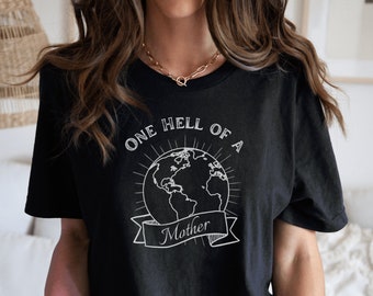 Puede incluir: Camiseta negra con un gráfico blanco de la Tierra con el texto "One Hell of a Mother" en ella.