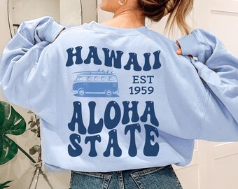Puede incluir: Sudadera azul claro con un gráfico retro de una furgoneta y el texto "HAWAII EST 1959 ALOHA STATE".