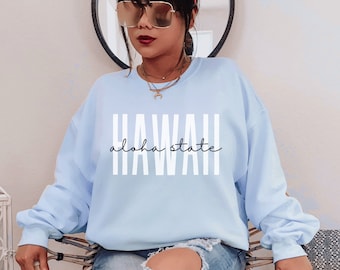Puede incluir: Una sudadera azul claro con el texto "HAWAII aloha state" impreso en blanco.