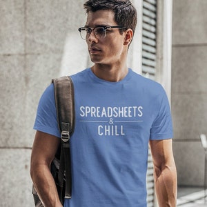 Könnte beinhalten: Ein Mann trägt ein hellblaues T-Shirt mit dem Text "SPREADSHEETS & CHILL" in Weiß. Er trägt einen braunen Lederrucksack und hat einen ernsten Gesichtsausdruck.