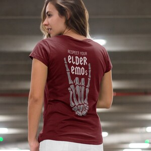 K&ouml;nnte beinhalten: Ein maroonfarbenes T-Shirt mit einer Skeletthand, die das Rock'n'Roll-Zeichen macht. Der Text auf dem Shirt lautet "Respect Your Elder Emos".