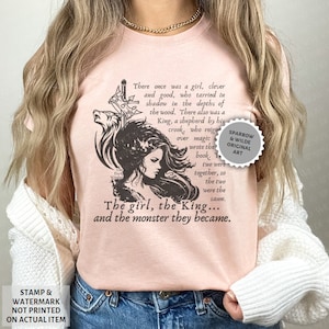Puede incluir: Una camiseta rosa con una ilustraci&oacute;n en blanco y negro de una ni&ntilde;a y un lobo. El texto en la camiseta dice: "There once was a girl, clever and good, who tarried in shadow in the depths of the wood. There also was a King, a shepherd by his crook, who reigned over magic & wrote the book. The two were together, so the two were the same. The girl, the King... and the monster they became."