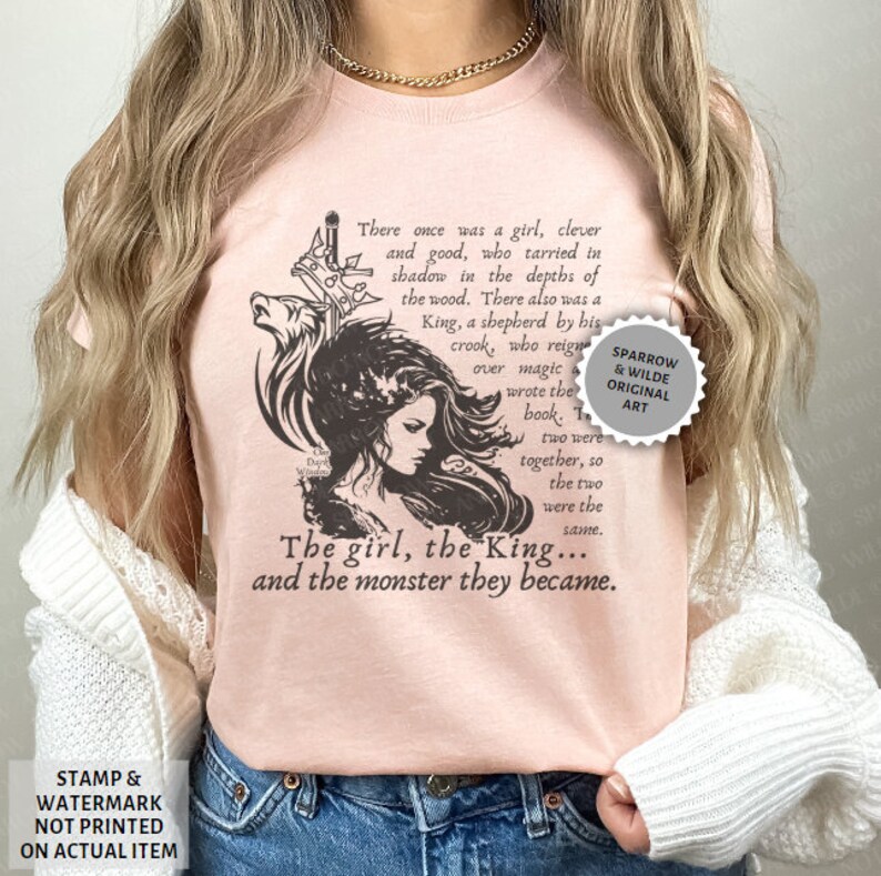 Puede incluir: Una camiseta rosa con una ilustraci&oacute;n en blanco y negro de una ni&ntilde;a y un lobo. El texto en la camiseta dice: "There once was a girl, clever and good, who tarried in shadow in the depths of the wood. There also was a King, a shepherd by his crook, who reigned over magic & wrote the book. The two were together, so the two were the same. The girl, the King... and the monster they became."