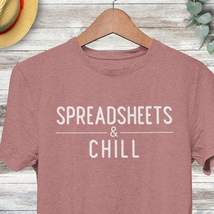 Puede incluir: Una camiseta de color rosa p&aacute;lido con el texto "SPREADSHEETS & CHILL" impreso en blanco.
