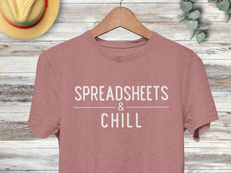 Puede incluir: Una camiseta de color rosa p&aacute;lido con el texto "SPREADSHEETS & CHILL" impreso en blanco.