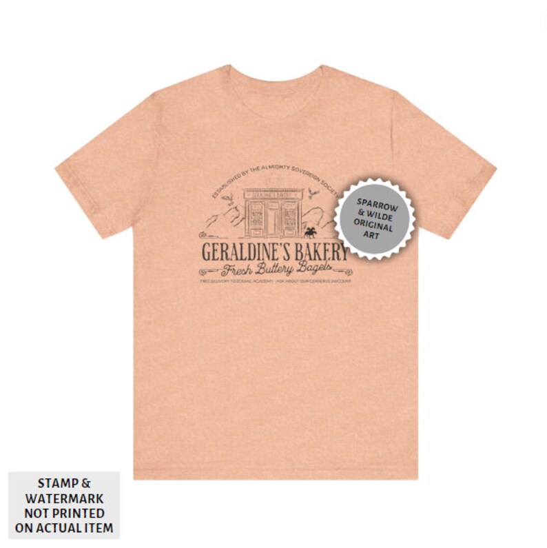 May include: A peach-coloured t-shirt featuring a black and white illustration of a bakery called "Geraldine's Bakery: Fresh Buttery Bagels". The illustration includes a shop front with a sign that reads "Geraldine's Bakery", a mountain range, and two birds. The text "Established by the Almonty Sovereign Society" appears above the illustration. The text "Free Delivery to Edgar Academy - Ask About Supernumerary Discount" appears below the illustration. A grey circle with the text "Sparrow & Wilde Original Art" appears in the top right corner of the image.