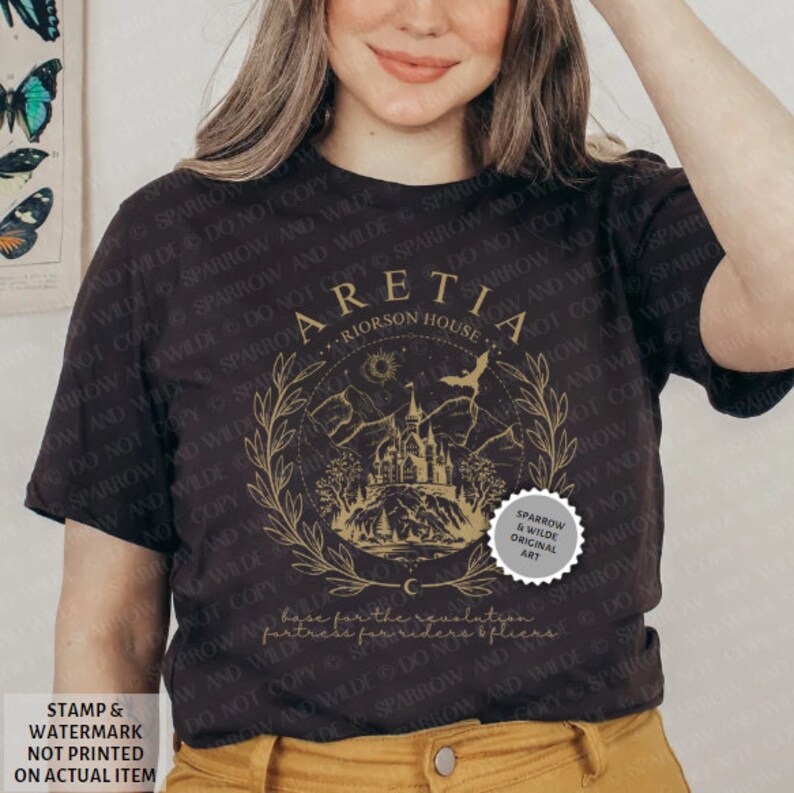 Może przedstawiać: Czarny T-shirt z złotym wzorem graficznym przedstawiającym zamek, drzewa i nietoperza. Na wzorze nadrukowany jest tekst "ARETIA - RIORSON HOUSE". Wz&oacute;r otoczony jest wieńcem z liści. W prawym dolnym rogu wzoru znajduje się mały srebrny okrąg z tekstem "SPARROW & WILDE ORIGINAL ART".