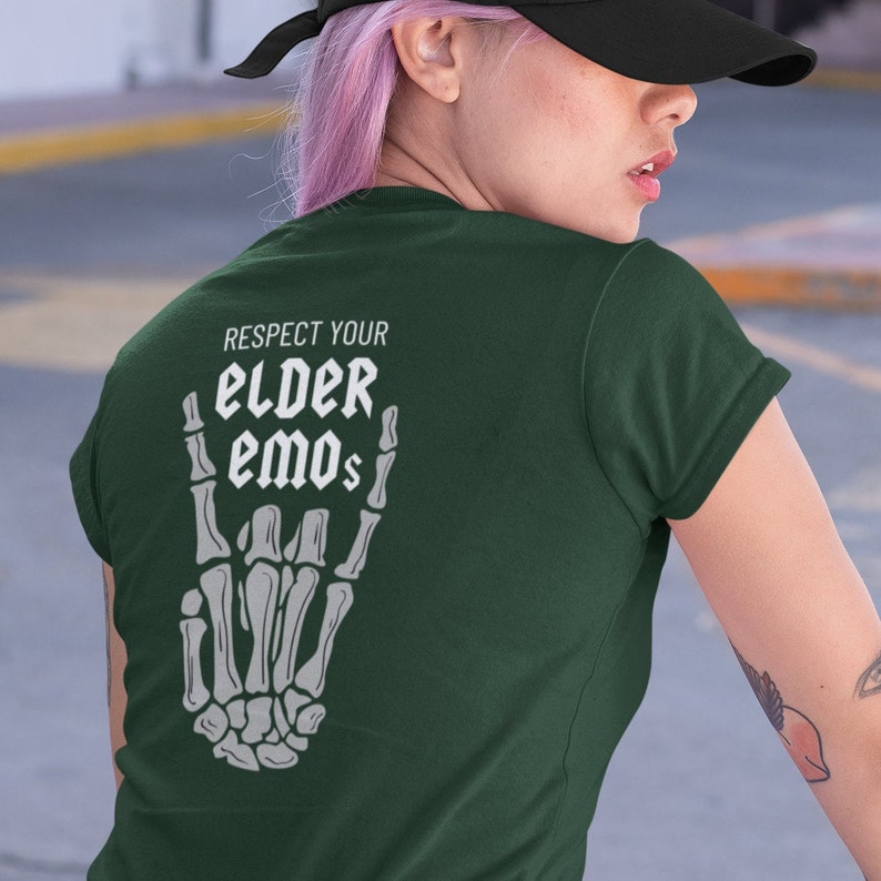 K&ouml;nnte beinhalten: Ein dunkelgr&uuml;nes T-Shirt mit einer wei&szlig;en Skeletthand, die das Rock'n'Roll-Zeichen macht. Der Text "Respect Your Elder Emos" ist auf das Shirt gedruckt.