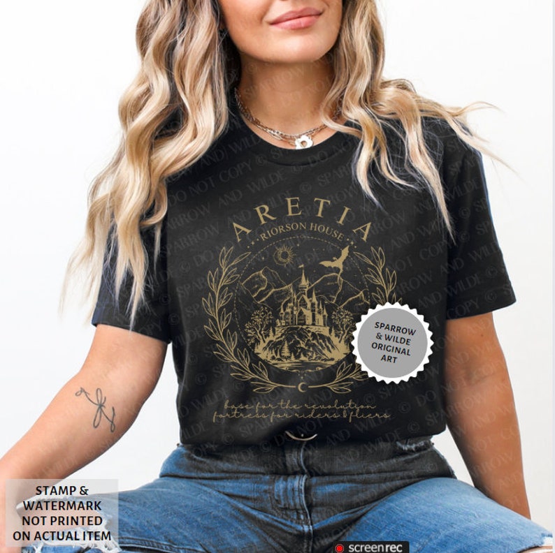 Może przedstawiać: Czarny T-shirt z złotym wzorem graficznym przedstawiającym zamek, g&oacute;ry i p&oacute;łksiężyc. Na wzorze nadrukowany jest tekst "Aretia - Riorson House". Wz&oacute;r otoczony jest wieńcem z liści. Na złotej okrągłej naklejce nadrukowany jest tekst "Sparrow & Wilde Original Art".