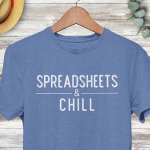 Puede incluir: Una camiseta azul con el texto "SPREADSHEETS & CHILL" impreso en blanco.