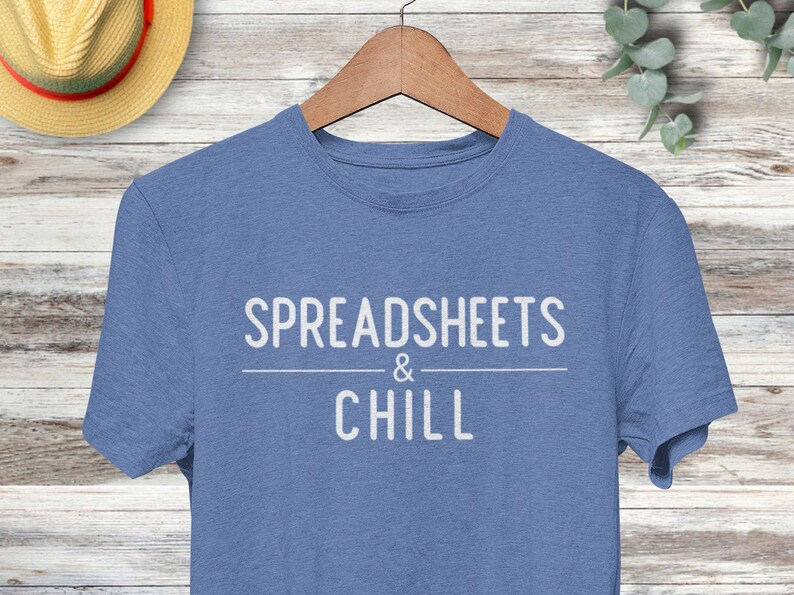 Puede incluir: Una camiseta azul con el texto "SPREADSHEETS & CHILL" impreso en blanco.