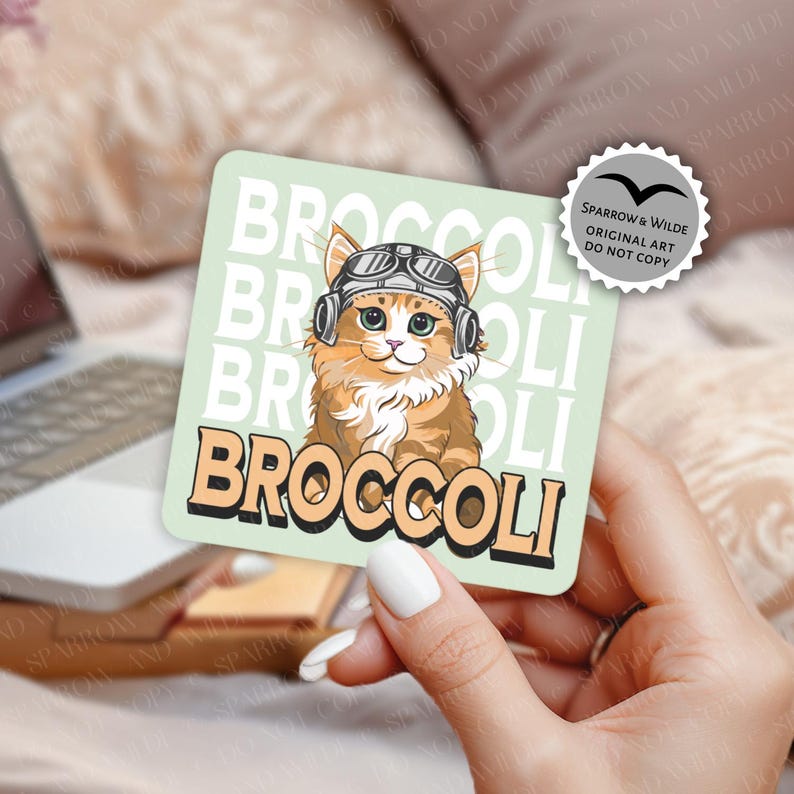 May include: Square sticker with a light green background featuring a cartoon cat wearing aviator goggles and headphones. The word "BROCCOLI" is printed in a retro font. The sticker also has the text "SPARROW & WILDE ORIGINAL ART DO NOT COPY".