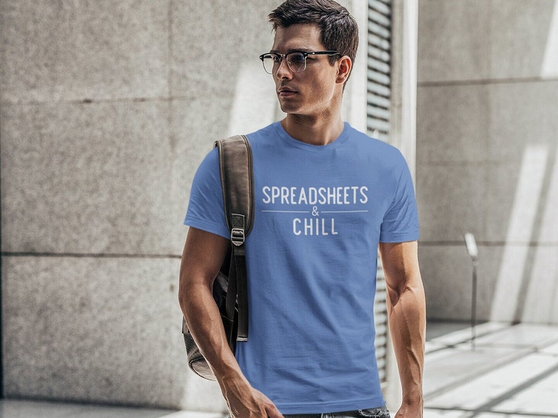 Puede incluir: Un hombre con una camiseta azul claro con el texto "SPREADSHEETS & CHILL" en blanco. Lleva una mochila de cuero marr&oacute;n y tiene una expresi&oacute;n seria en la cara.
