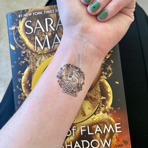 May include: A close-up of a person's wrist with a temporary tattoo of a unicorn with a floral wreath and the text "Jelly Jubilee". The tattoo is on the left wrist and the person is wearing green nail polish on their right hand.