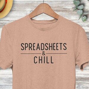 Puede incluir: Una camiseta marr&oacute;n claro con el texto "SPREADSHEETS & CHILL" impreso en negro.