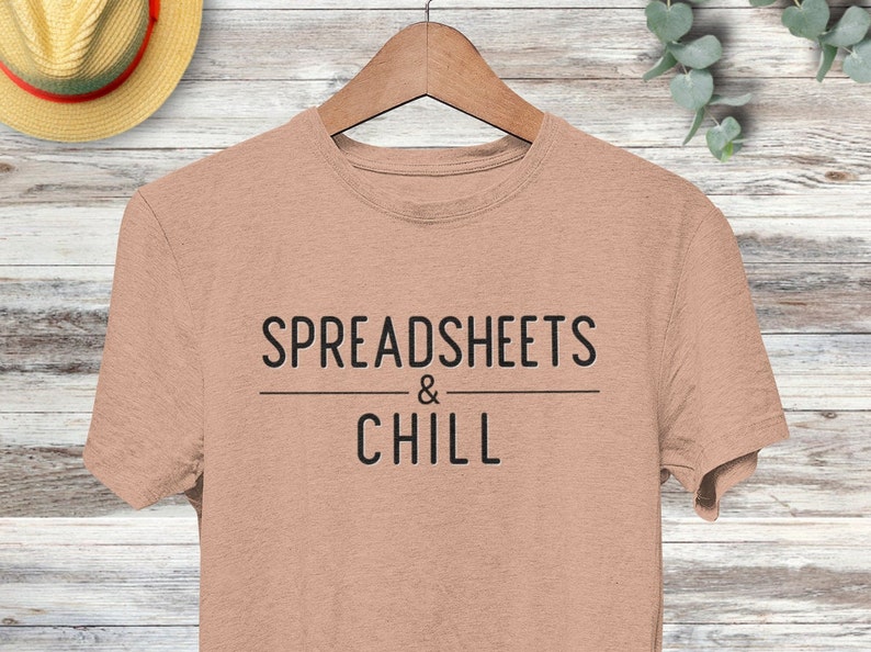 Puede incluir: Una camiseta marr&oacute;n claro con el texto "SPREADSHEETS & CHILL" impreso en negro.