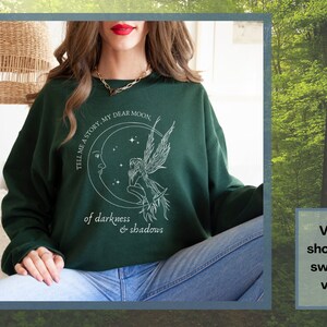 Op de afbeelding: Groen sweatshirt met een witte afbeelding van een fee die op een halve maan zit met de tekst "TELL ME A STORY, MY DEAR MOON of darkness & shadows".