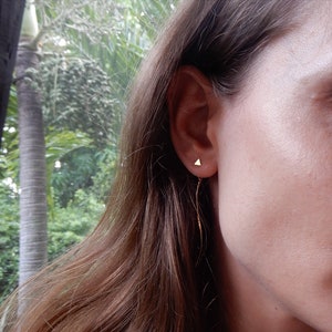 Peut inclure: Gros plan sur l'oreille d'une personne avec une boucle d'oreille en forme de triangle dorée et une longue chaîne dorée fine qui pend du bas.