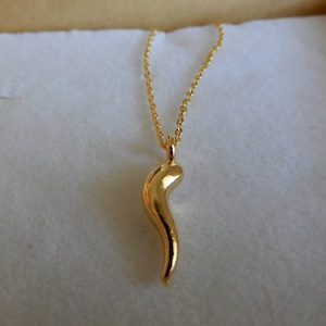 Puede incluir: Un collar de cadena de oro con un colgante de oro en forma de cuerno curvo.