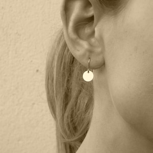 Peut inclure: Gros plan sur l'oreille d'une personne avec une petite boucle d'oreille ronde en or. La boucle d'oreille est de conception simple avec une finition lisse et polie.