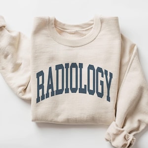 May include: A beige sweatshirt with the word "RADIOLOGY" printed in dark blue on the front.