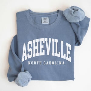 May include: A blue sweatshirt with the text 'ASHEVILLE NORTH CAROLINA' in white lettering.
