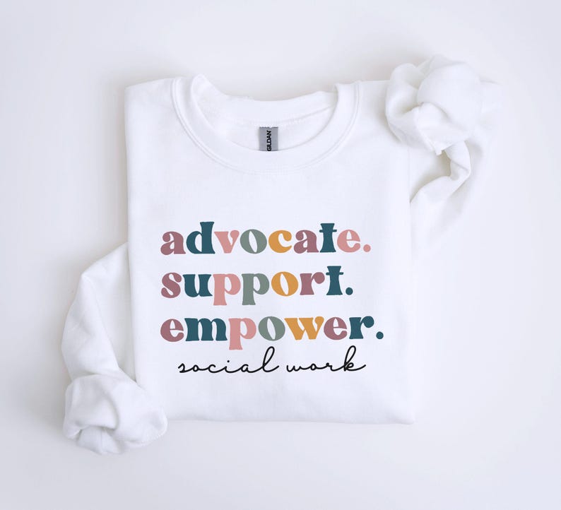 May include: White sweatshirt with the words "advocate. support. empower. social work" in a colorful, stacked design. The text is in various colors, including teal, pink, and gold. The sweatshirt has long sleeves and a crew neck.