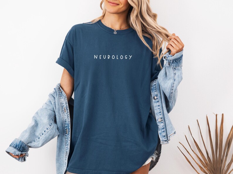 K&ouml;nnte beinhalten: Eine Frau tr&auml;gt ein dunkelblaues T-Shirt mit dem Wort "NEUROLOGY" in wei&szlig; auf der Vorderseite. Sie tr&auml;gt eine hellblaue Jeansjacke &uuml;ber dem Shirt.