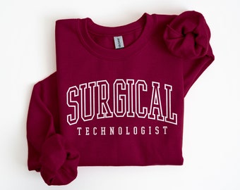 May include: Burgundy sweatshirt with white text that reads "SURGICAL TECHNOLOGIST" in a collegiate font.