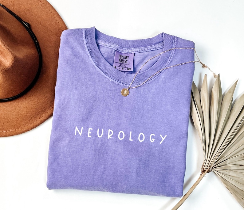 K&ouml;nnte beinhalten: Ein lavendelfarbenes T-Shirt mit dem Wort "NEUROLOGY" in Wei&szlig; auf der Vorderseite. Das Shirt ist aus weichem, bequemem Material und hat eine lockere Passform.