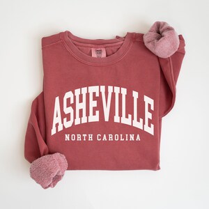 May include: A maroon sweatshirt with the text "ASHEVILLE NORTH CAROLINA" in white.