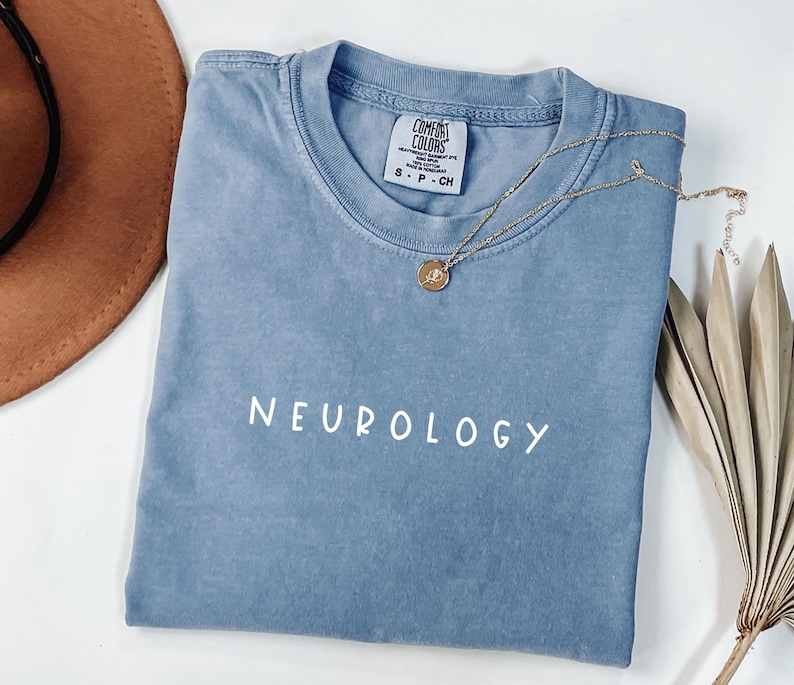 K&ouml;nnte beinhalten: Ein hellblaues T-Shirt mit dem Wort "NEUROLOGY" in wei&szlig; auf der Vorderseite. Das Shirt ist aus weichem, bequemem Material und hat eine lockere Passform.