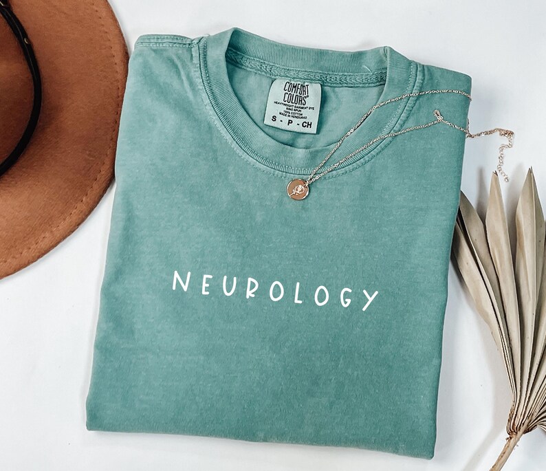K&ouml;nnte beinhalten: Ein tealgr&uuml;nes T-Shirt mit dem Wort "NEUROLOGY" in Wei&szlig; auf der Vorderseite. Das Shirt ist aus einem weichen, bequemen Material und hat eine lockere Passform.