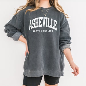 May include: A gray sweatshirt with the text "Asheville, North Carolina" printed in white.