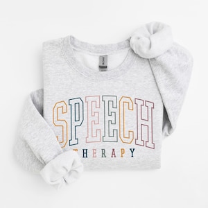 May include: A grey sweatshirt with the text "SPEECH THERAPY" in rainbow colours. The text is in a collegiate font style.