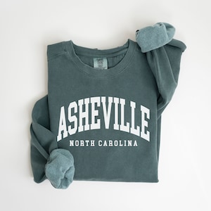 May include: A teal blue sweatshirt with the text "ASHEVILLE NORTH CAROLINA" in white.