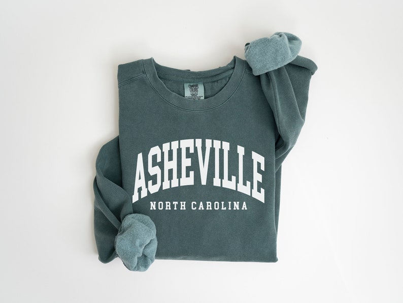 May include: A teal blue sweatshirt with the text "ASHEVILLE NORTH CAROLINA" in white.