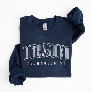 Peut inclure: Un sweat-shirt bleu marine avec le texte "ULTRASOUND TECHNOLOGIST" en blanc.
