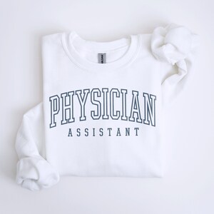 K&ouml;nnte beinhalten: Wei&szlig;er Pullover mit dem Text "PHYSICIAN ASSISTANT" in einer dunkelblauen College-Schrift.